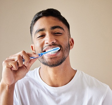 Man in white t-shirt brushing his teeth with blue and white toothbrush