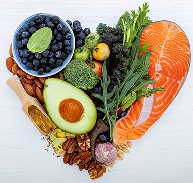 A variety of healthy foods arranged in a heart shape on a white wooden surface